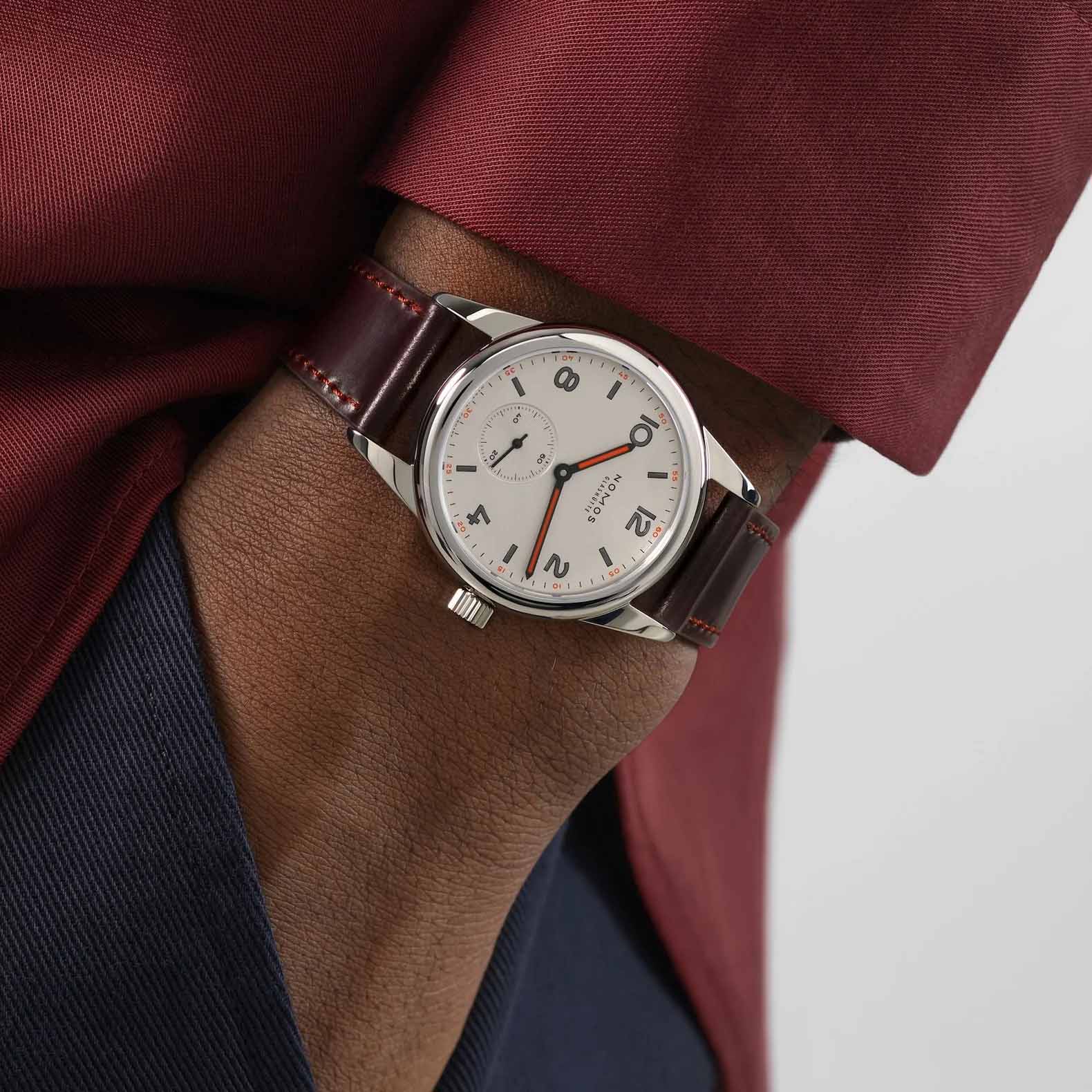 Man wearing NOMOS Glashütte Club 36mm watch with white silver-plated dial, black and red hands, and brown Horween leather strap