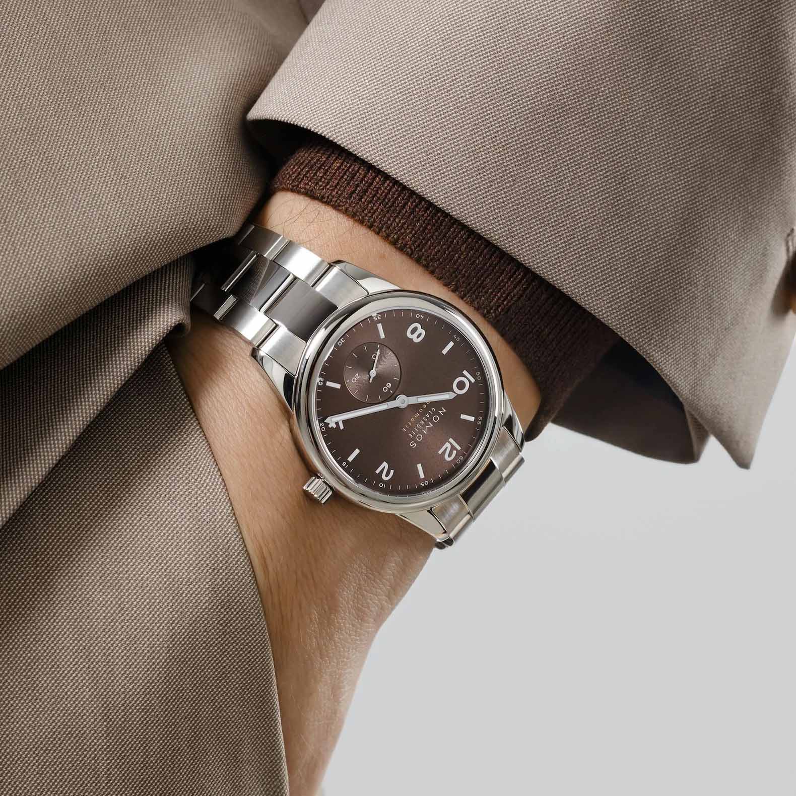 Man wearing NOMOS Glashütte Club Sport Neomatik 39mm watch with tabac brown sunburst dial, luminous hands, and stainless steel bracelet.