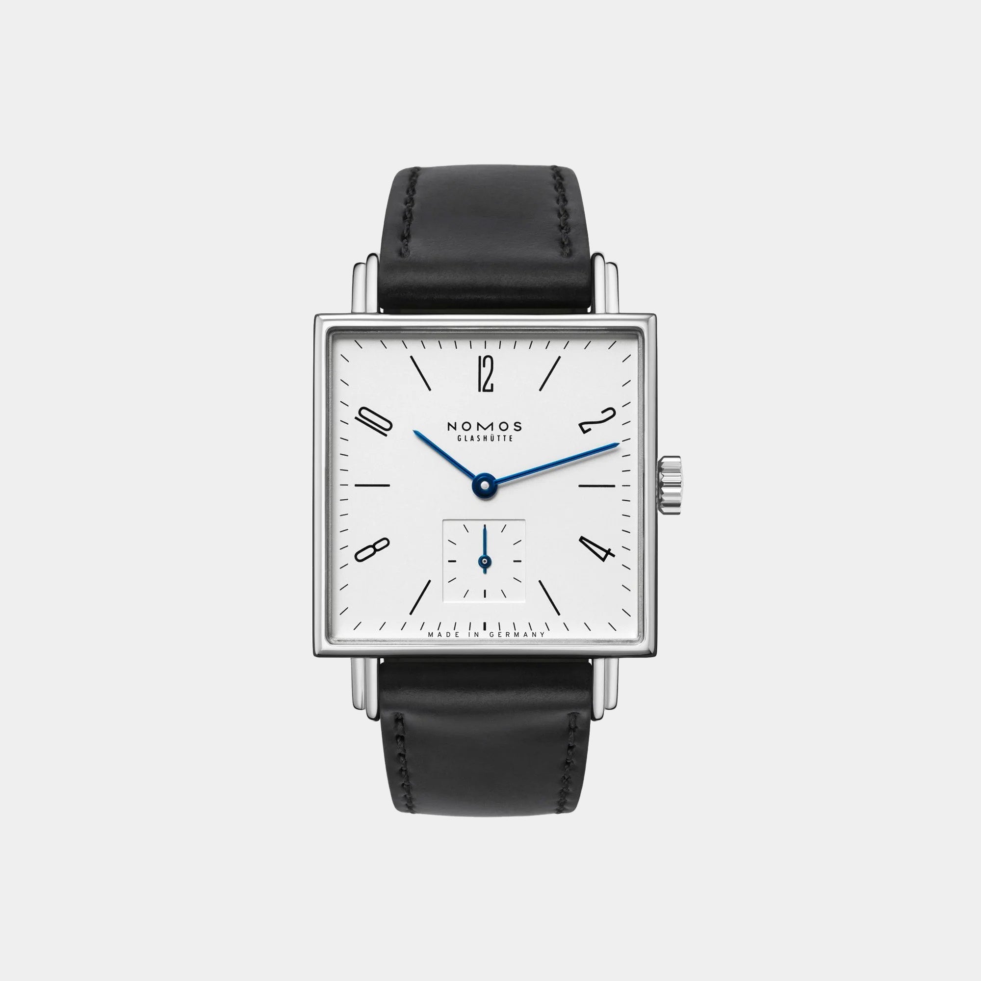 NOMOS Glashütte Tetra 29.5mm square watch with white dial, blue hands, and black Horween leather strap on grey background, front view.