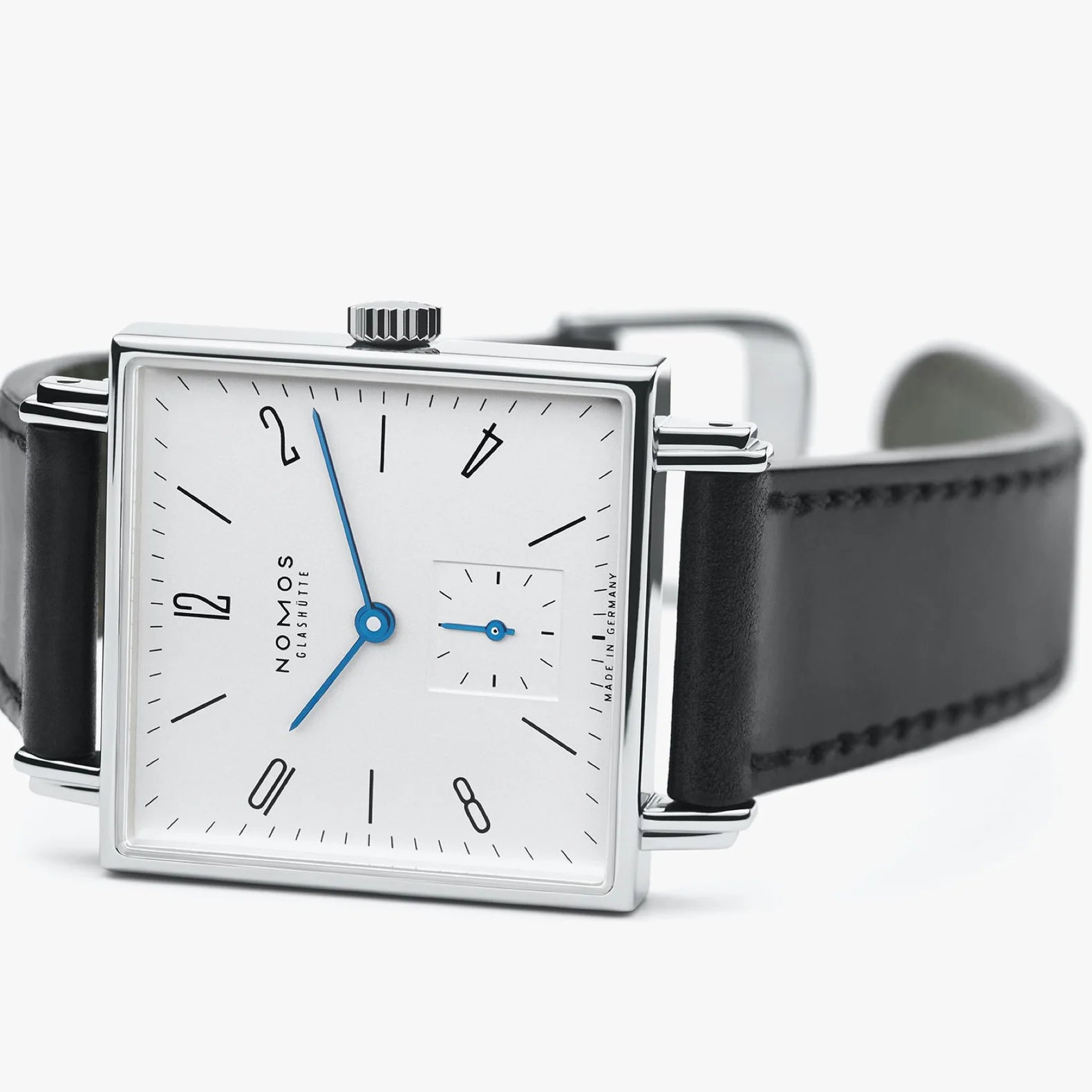 NOMOS Glashütte Tetra 29.5mm square watch with white dial, blue hands, and black Horween leather strap on white background, angled side view.