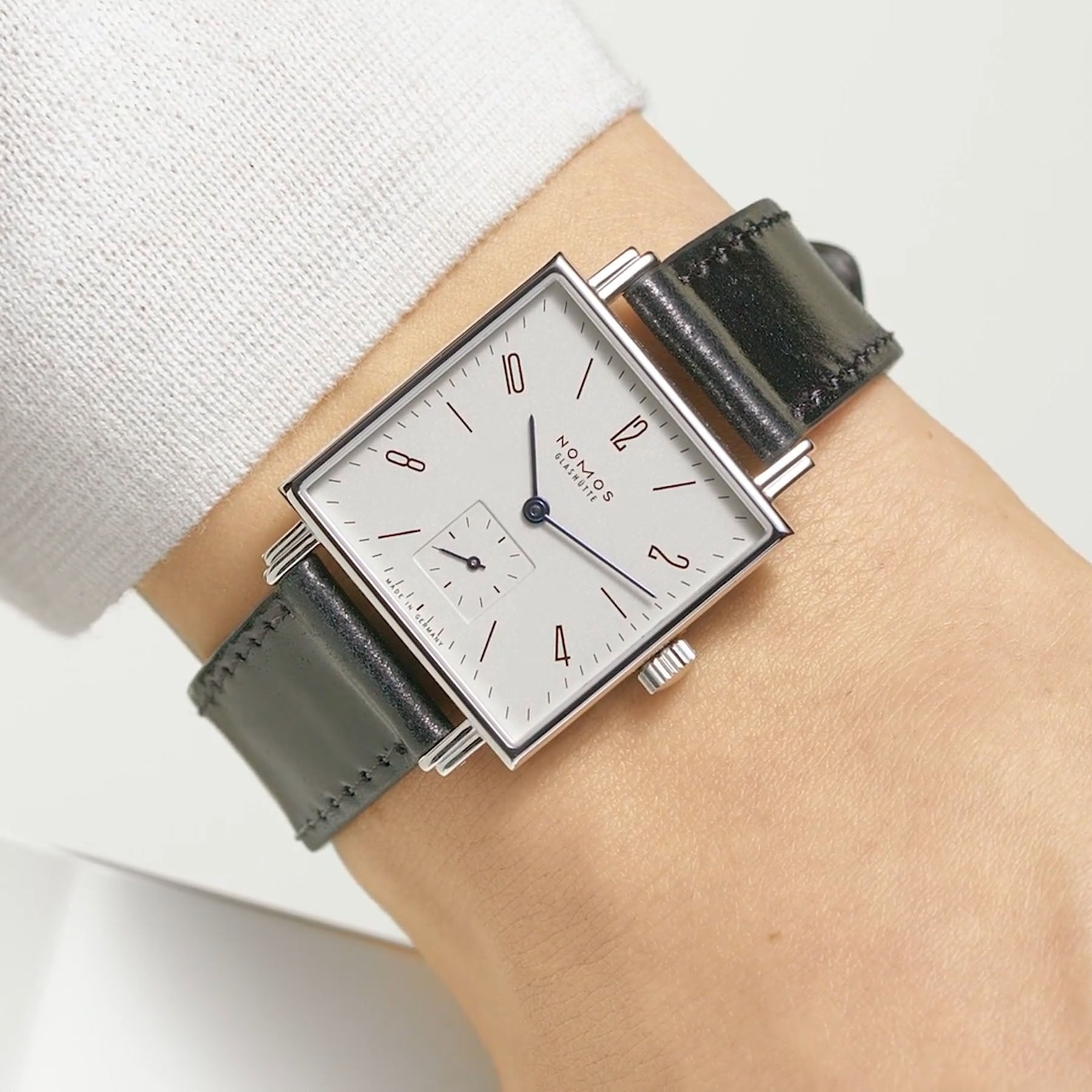 Man wearing NOMOS Glashütte Tetra 29.5mm square watch with white dial, blue hands, and black Horween leather strap