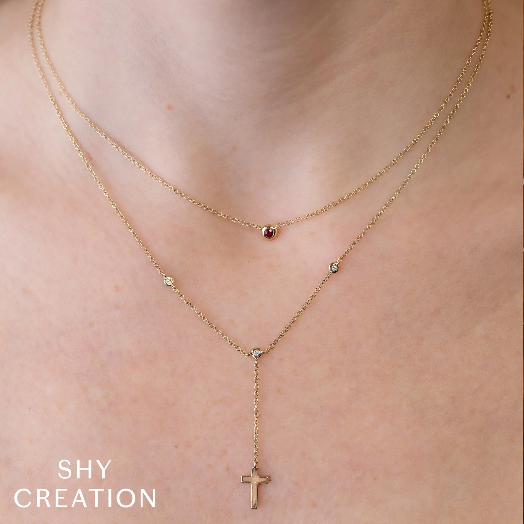 Layered 14K yellow gold chains with a petite ruby bezel pendant by Shy Creation on a model’s neck (lifestyle shot).