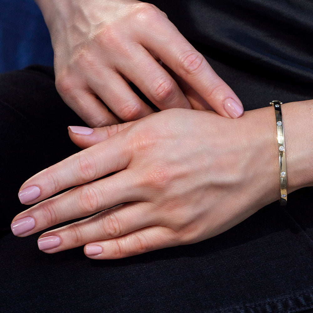 Woman wearing yellow gold bezel set diamond bangle bracelet, closeup of wrist