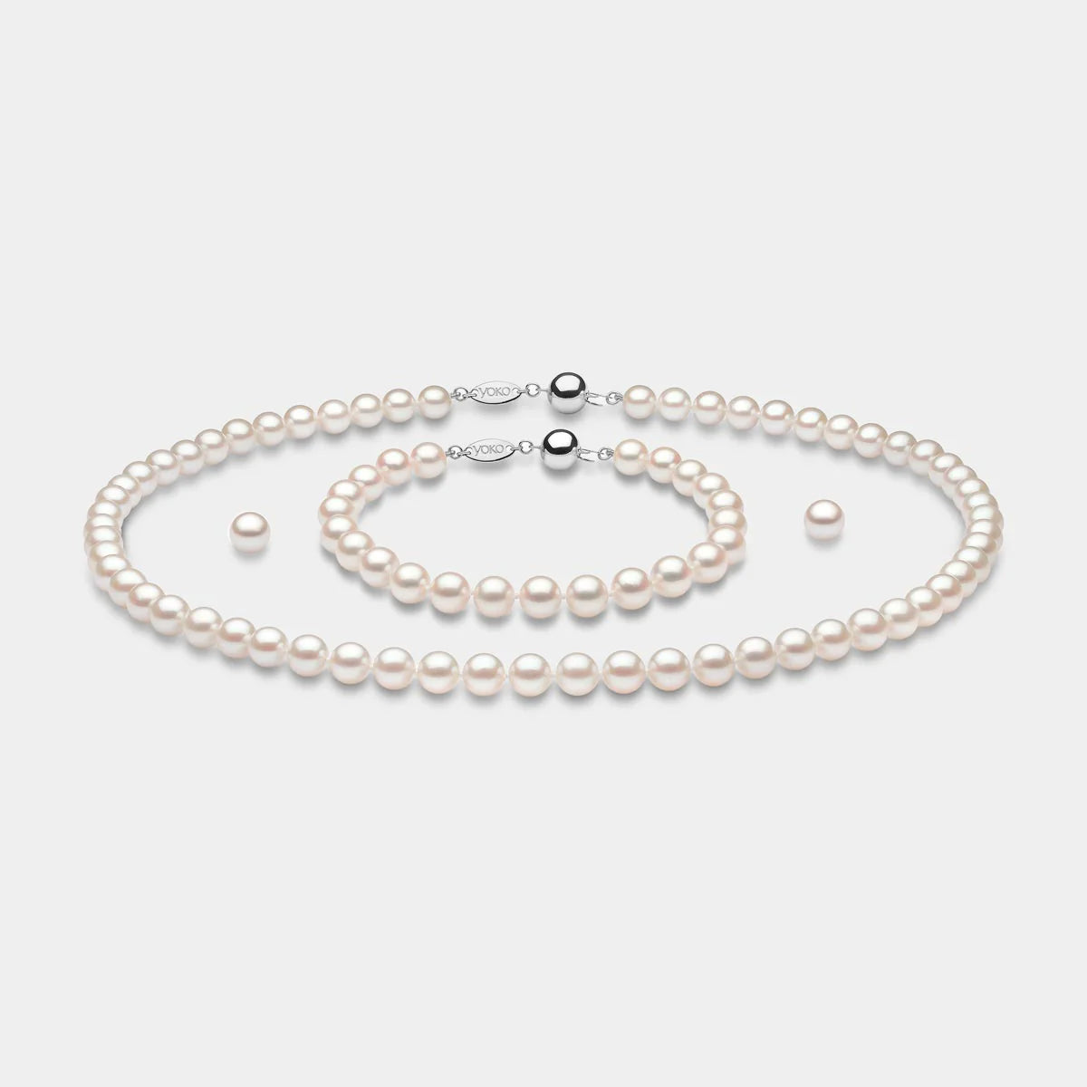 Pearl necklace, bracelet, and earrings set on a light gray background