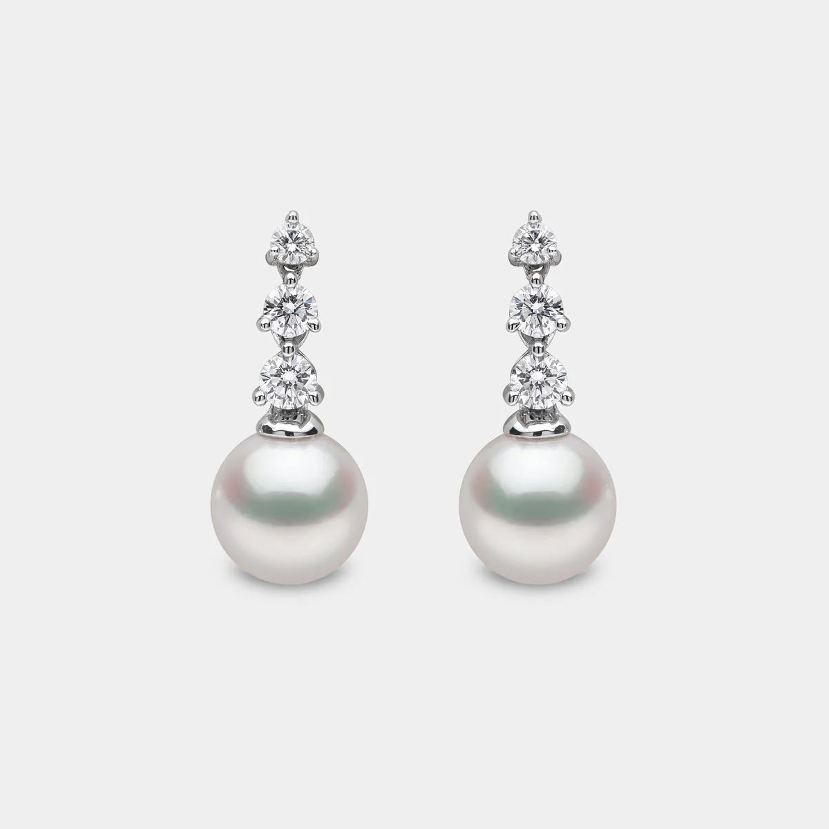 White gold pearl and diamond drop earrings on grey background, front view