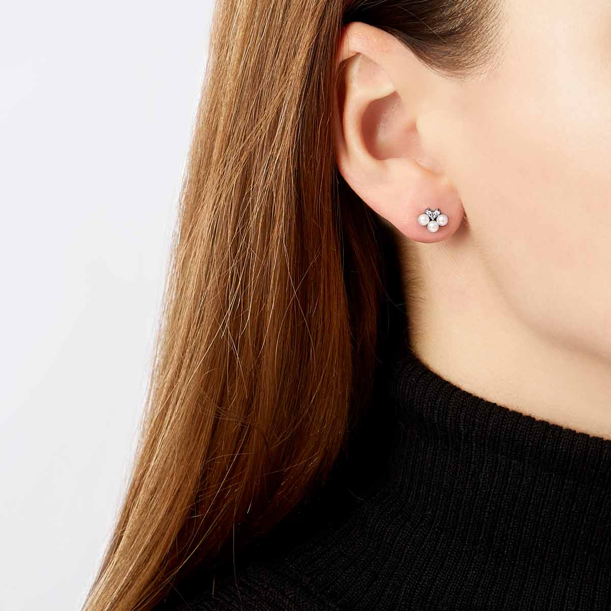 Close-up of a person wearing a white gold earring with pearls and diamond accents