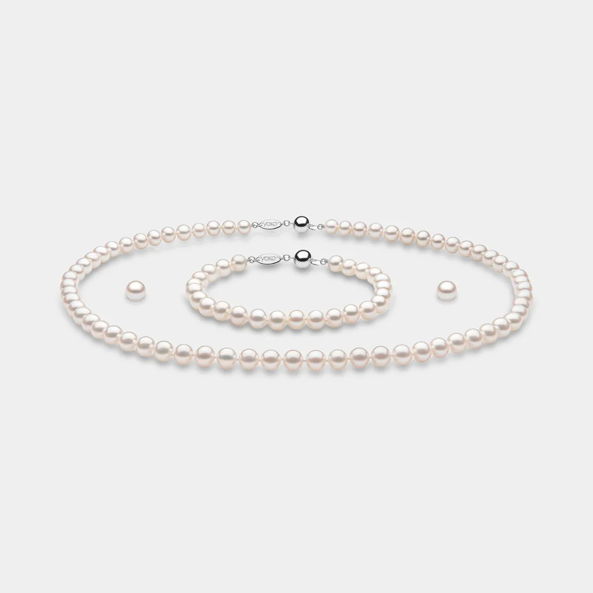 White gold pearl necklace, bracelet, and earrings set on grey background