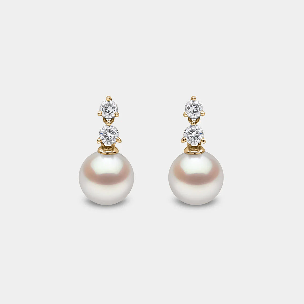 Yellow gold pearl and diamond drop earrings on grey background, side angle view