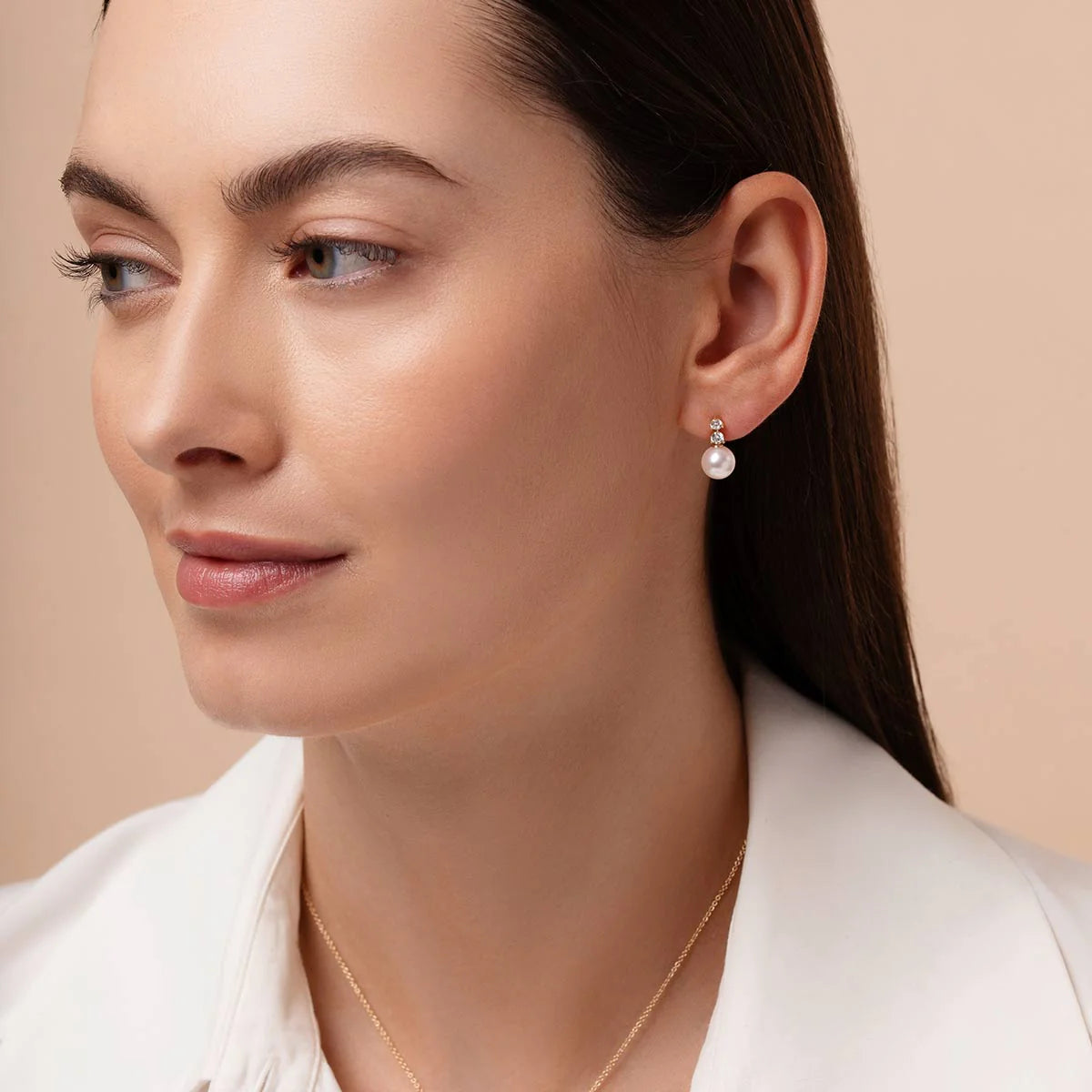 Close-up of a woman wearing pearl earrings with a neutral background